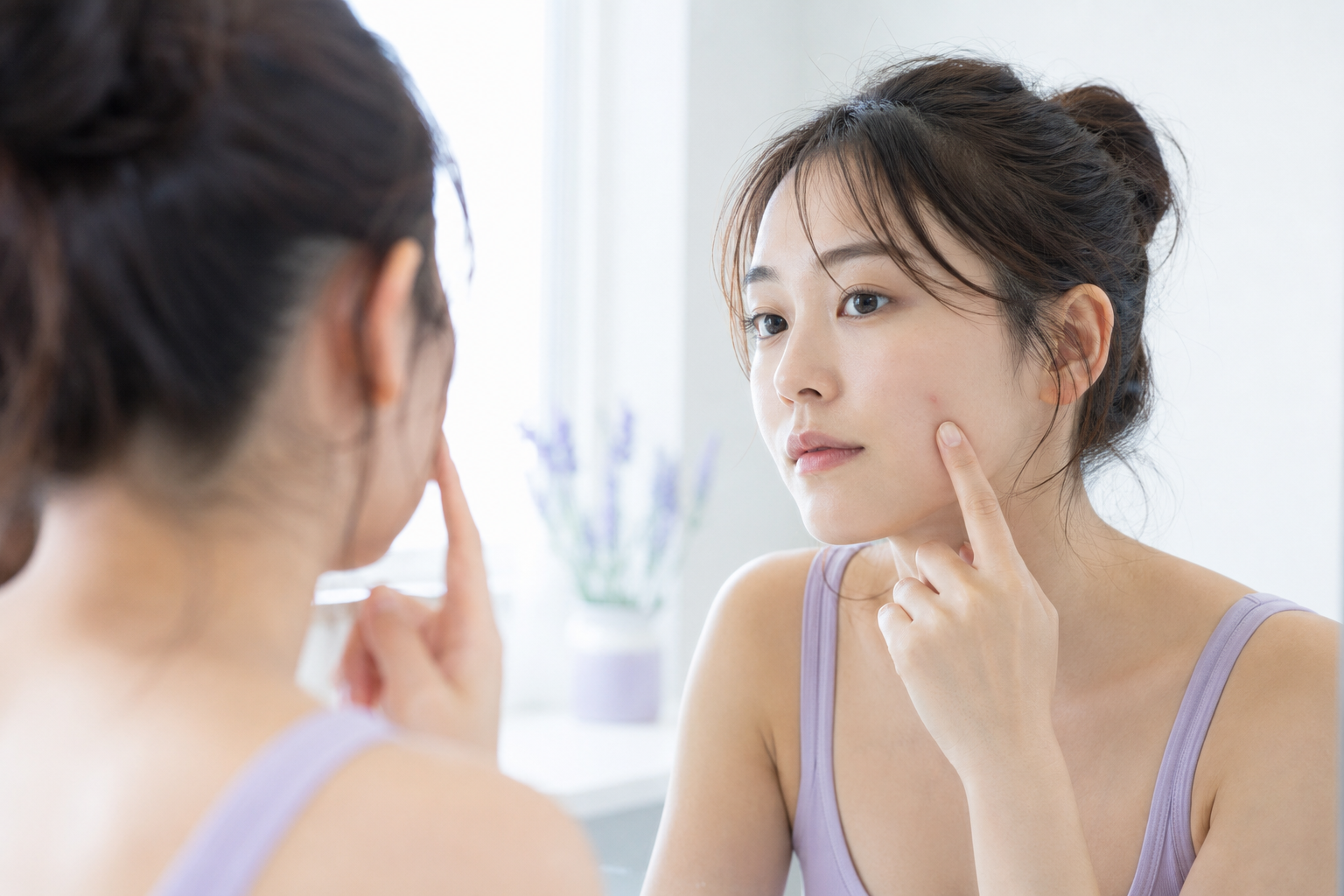 鏡を見ながら頬のニキビを確認する女性