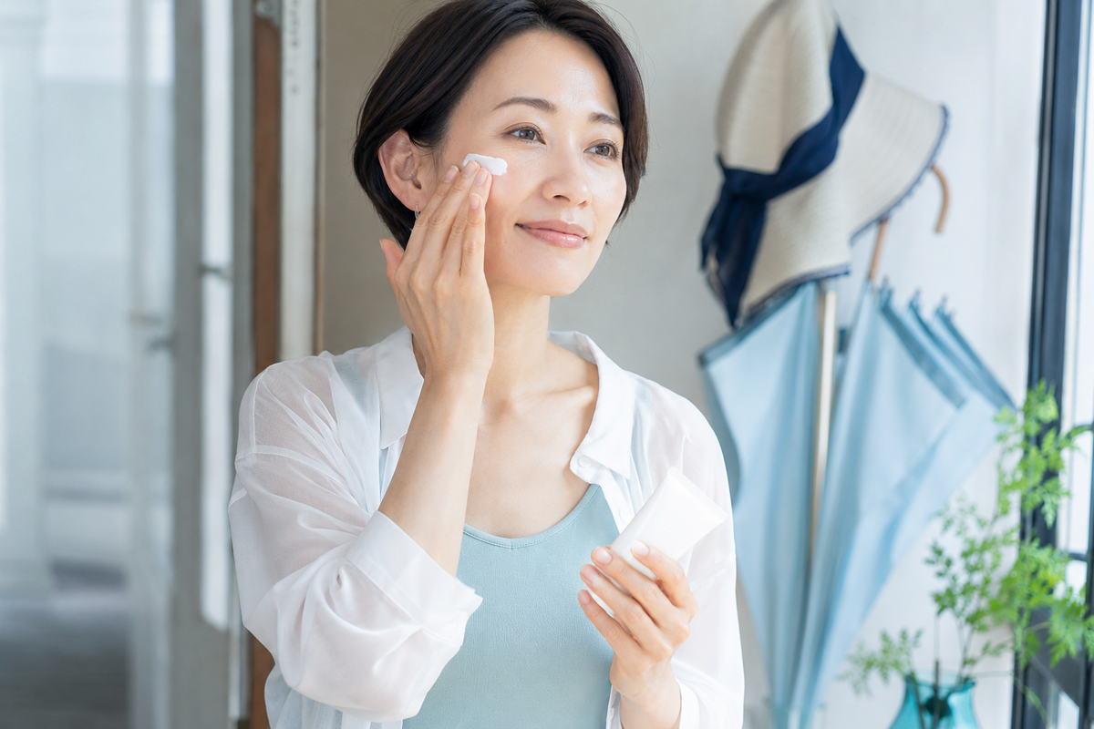 外出前に日焼け止めを塗り、帽子と日傘を準備する日本人女性